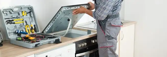 Cooktop repair technician lifting a built-in stovetop for service in Philadelphia, PA