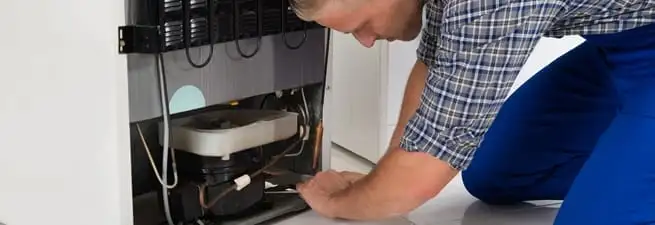 Refrigerator repair technician servicing the compressor and condenser area in Philadelphia, PA