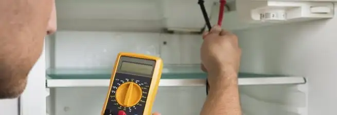 Refrigerator repair technician testing electrical components with a multimeter in Philadelphia, PA